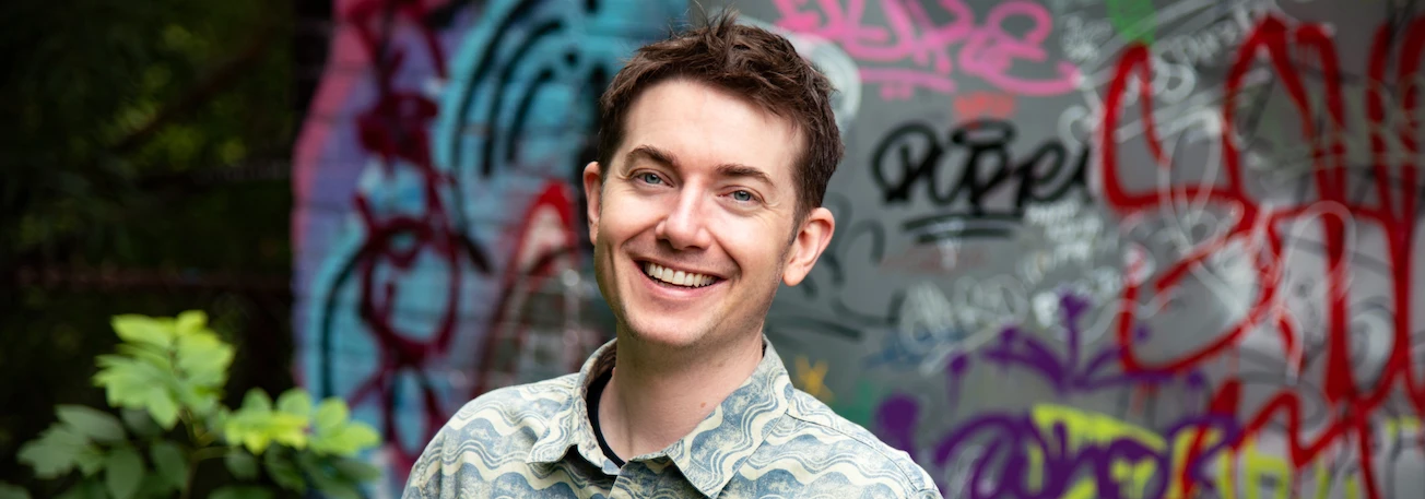 Michael Curren smiling warmly in front of a wall covered in graffiti.